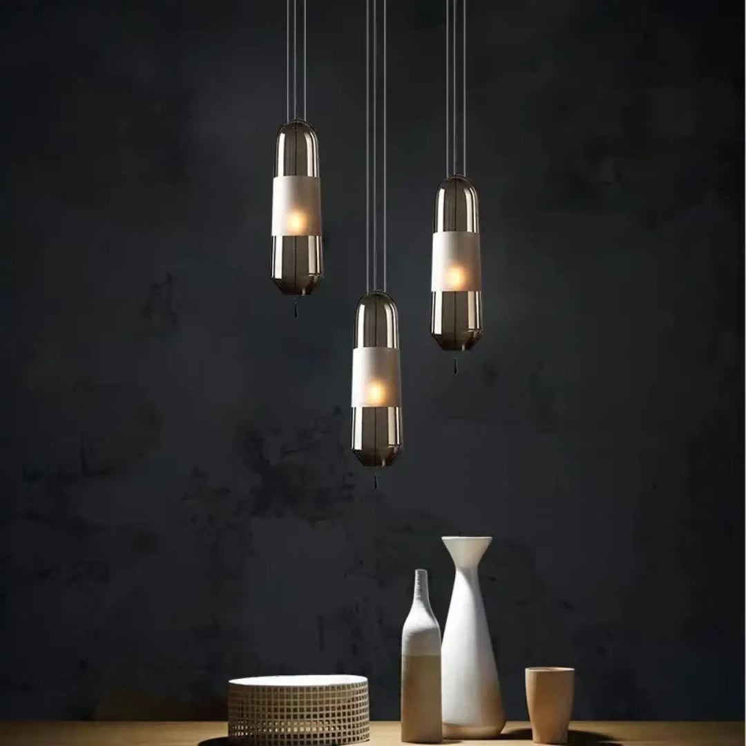 Trois suspensions luminaires oxya en métal avec abat-jours en verre chaud suspendues devant un mur texturé sombre