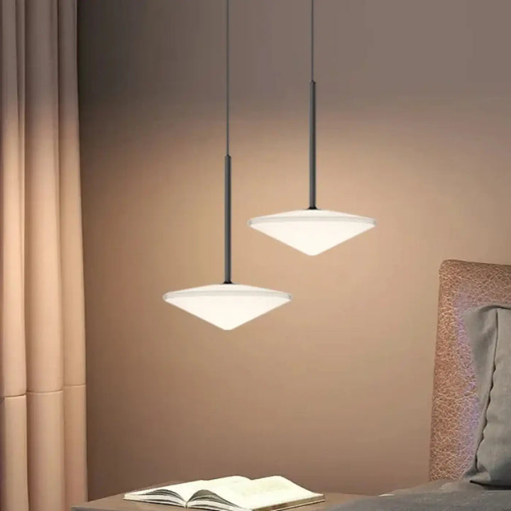 Deux suspensions luminaires moderns avec verre blanc en forme de diamant et courbes délicates au-dessus d’une table de chevet