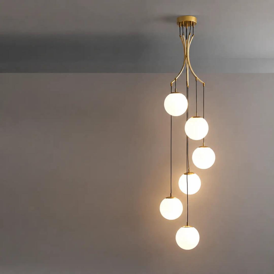 Suspension luminaire umami en laiton avec cinq globes en verre blanc disposés en cascade et lumineux