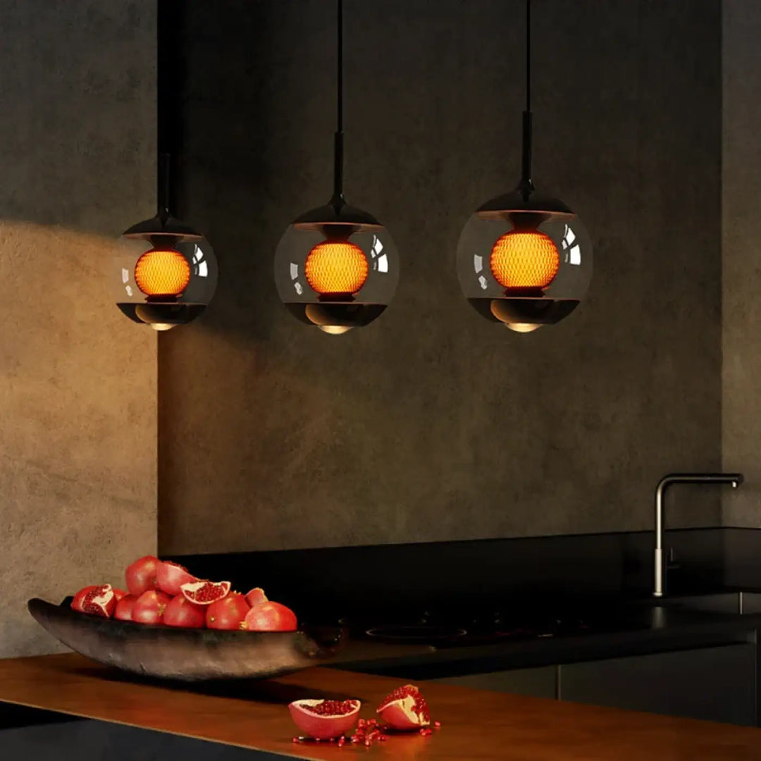 Trois suspensions luminaires nexus en verre clair avec intérieur orange chaud et luminosité variable au-dessus d’un comptoir