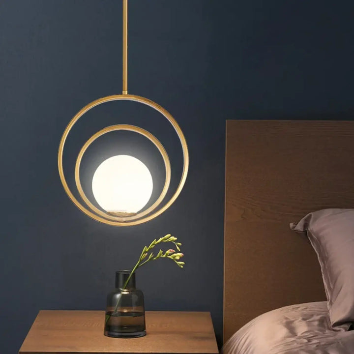 Suspension luminaire élégante lumienia en ton or avec deux anneaux concentriques et ampoule sphérique lumineuse