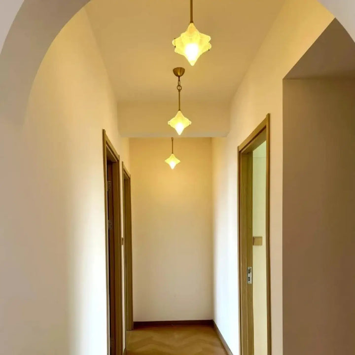 Trois suspensions luminaires petales en verre transparent aux tons chauds offrent un éclairage doux dans un couloir