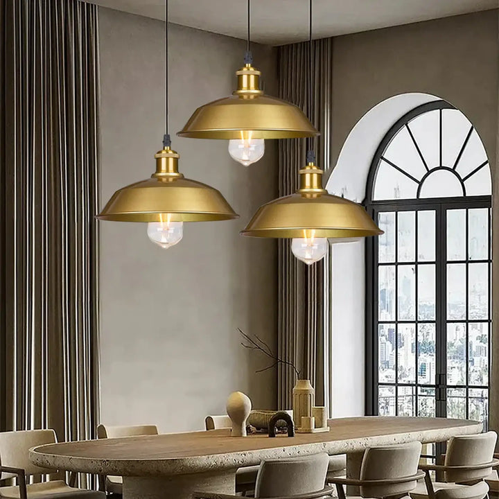 Trois suspensions luminaire industrielle dorée en laiton avec abat-jour en dôme et ampoules visibles au-dessus d’une table