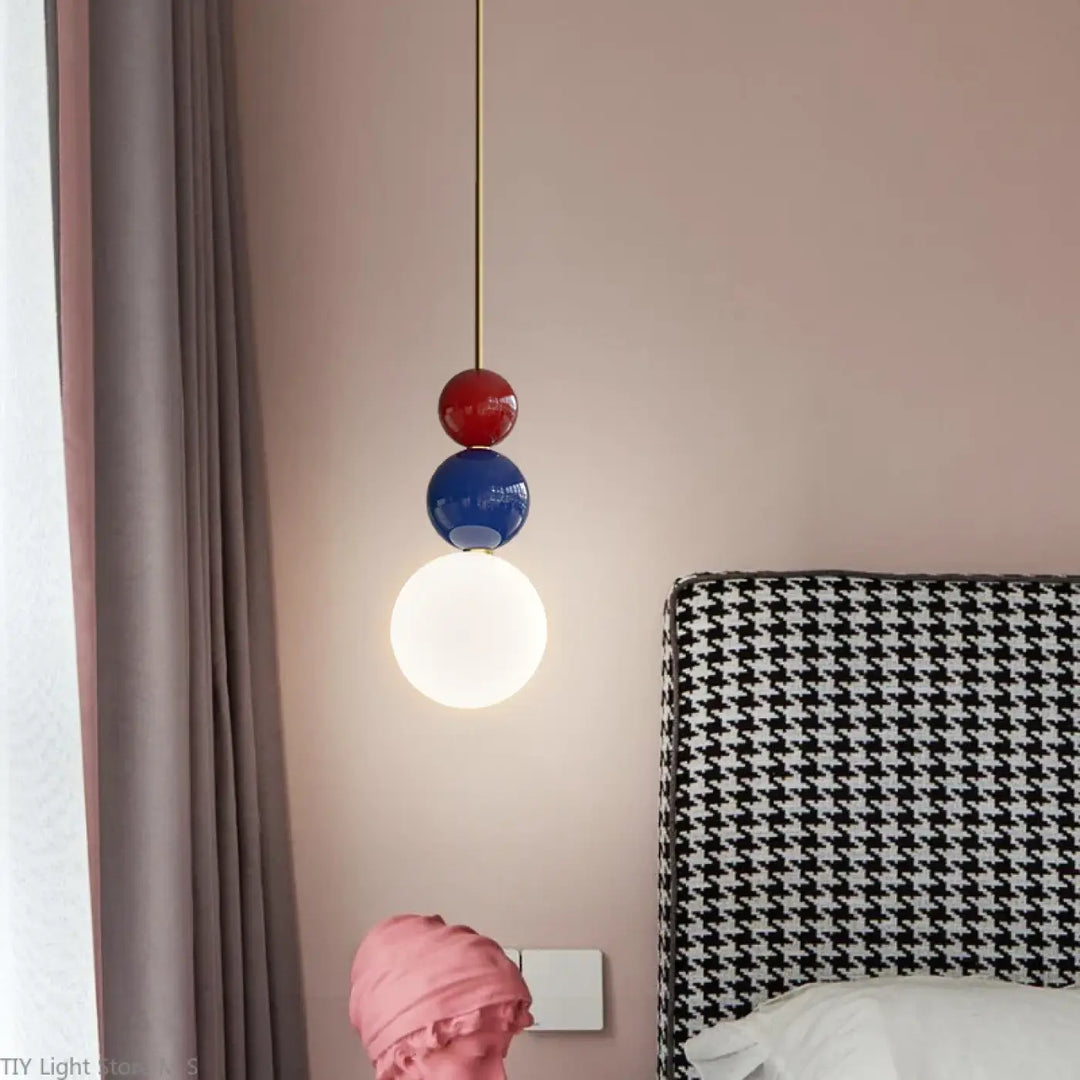 Suspension luminaire moderne resinia avec trois globes empilés rouge bleu blanc suspendus sur cordon doré au-dessus dune tête de lit pied-de-poule