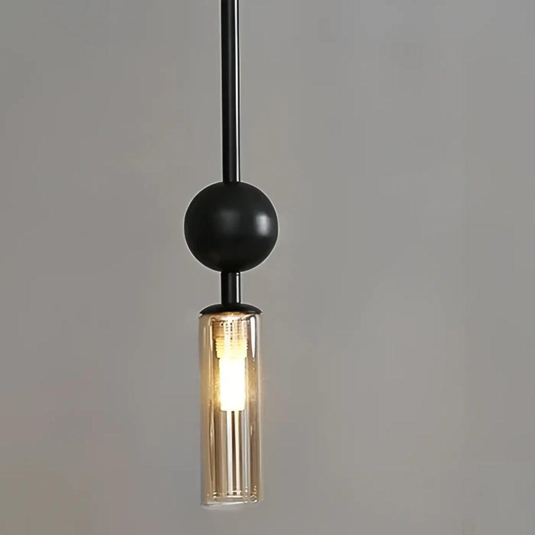 Suspension luminaire krysta avec boule métallique noire et cylindre en verre clair abritant une ampoule éclairée