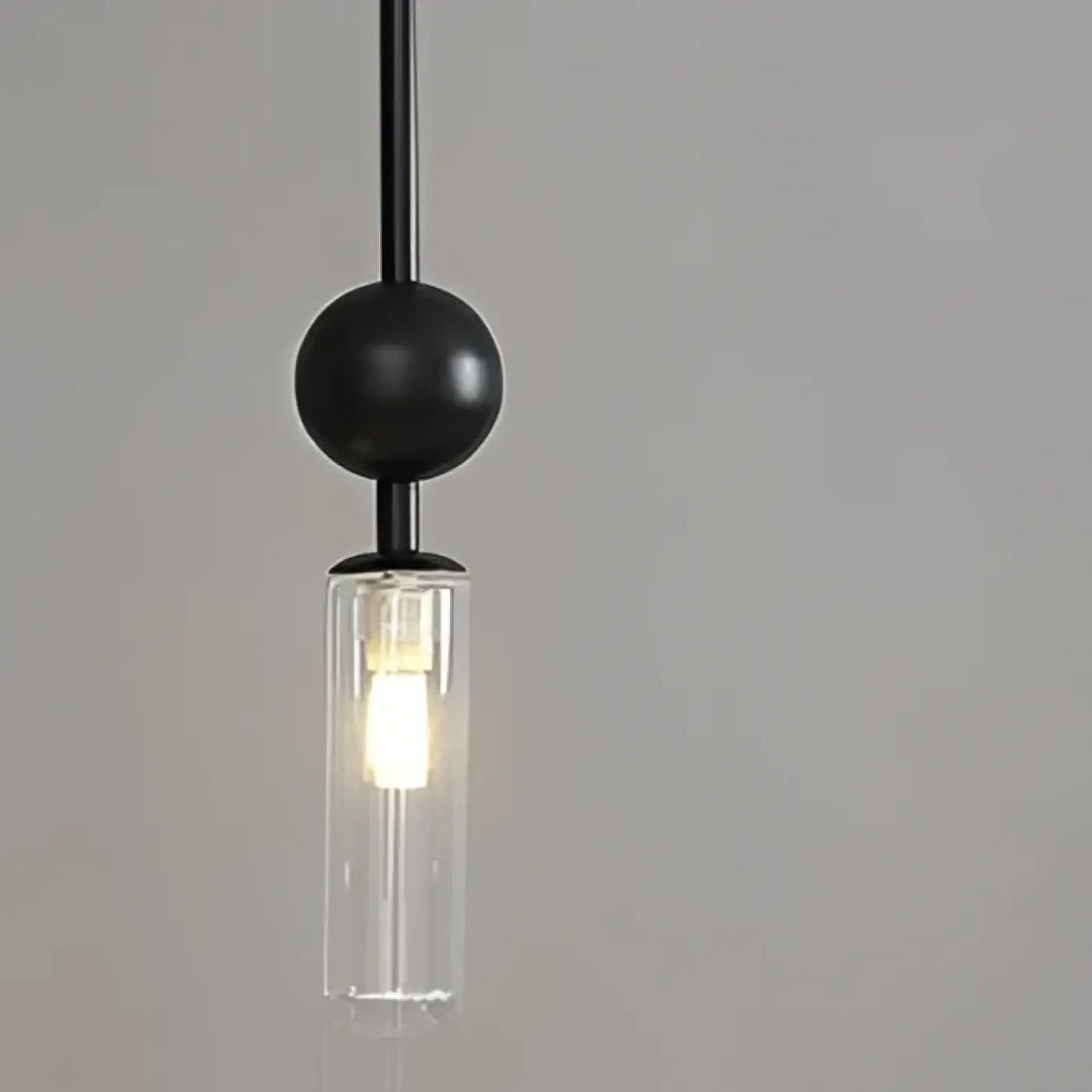 Suspension luminaire krysta avec boule métallique noire et cylindre en verre transparent abritant une ampoule allumée