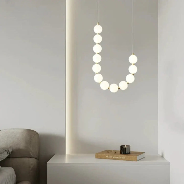 Suspension luminaire perita avec perles blanches sphériques givrés disposées en ligne courbée pour une ambiance douce