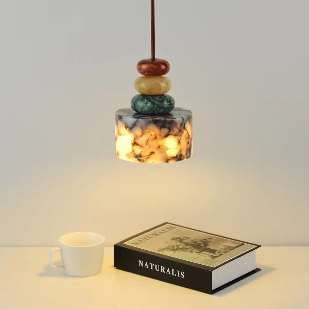 Suspension luminaire gaïa avec abat-jour cylindrique en verre pierre marbrée ambré et cordon sombre au-dessus de perles minérales colorées