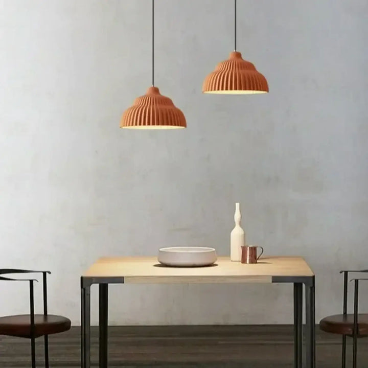 Deux suspensions luminaire plissée terracotta en terre cuite à nervures suspendues au-dessus d’une table en bois