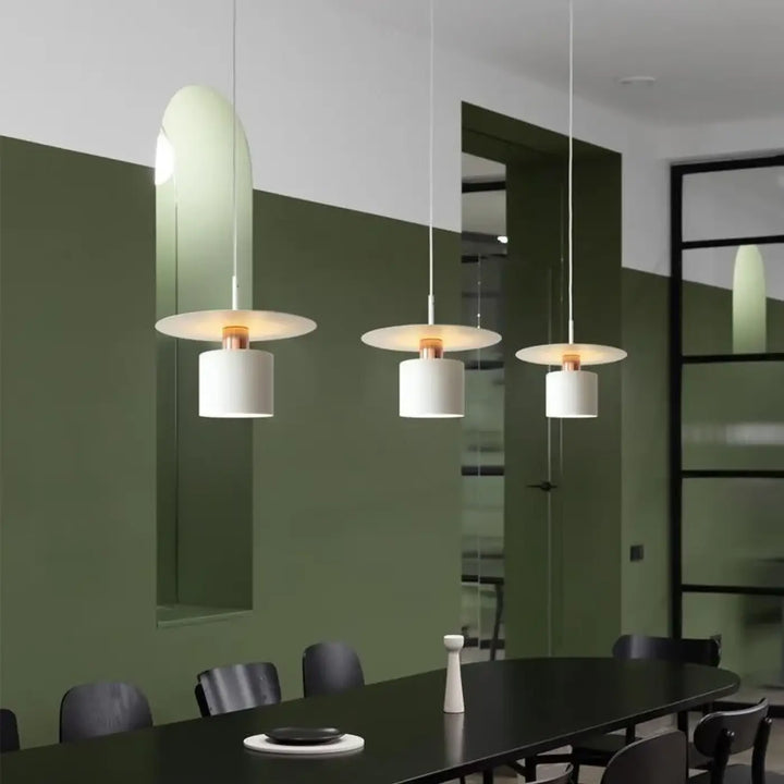 Suspension luminaire bougy avec trois suspensions raffinées en verre incurvé et abat-jour cylindrique blanc au-dessus d’une table sombre