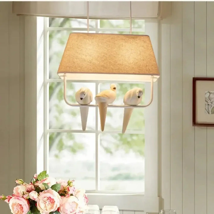Suspension luminaire rectangulaire beige en liège avec trois oiseaux en céramique blanche perchés sur une structure métallique