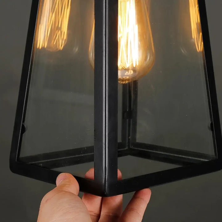 Black metal-framed suspension luminaire jardi with clear glass panels and a glowing filament bulb luminaire rétro-industriel