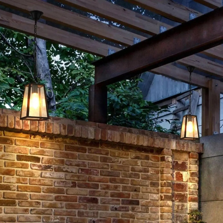 Suspension luminaire jardi avec lanternes en verre à tons chauds suspendues à une pergola en bois éclairant un mur en briques