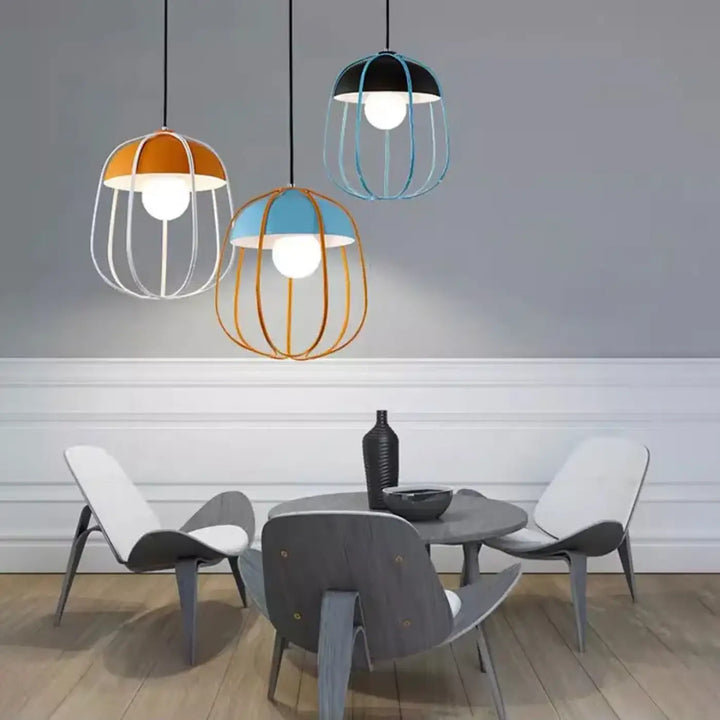 Trois suspension luminaire caldera avec cadres en fil orange bleu et noir au-dessus d’une table à manger