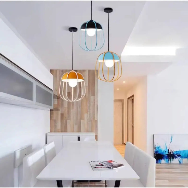 Suspension luminaire caldera avec trois suspensions en fil métallique noir bleu et or au-dessus d’une table à manger blanche