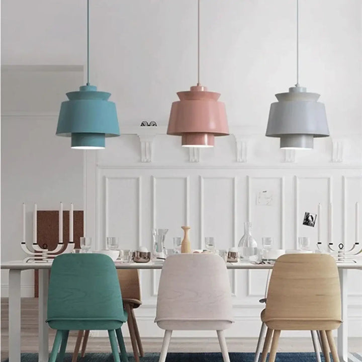 Suspension luminaire pendila avec trois suspensions pastel à abat-jours cylindriques superposés au-dessus d’une table à manger
