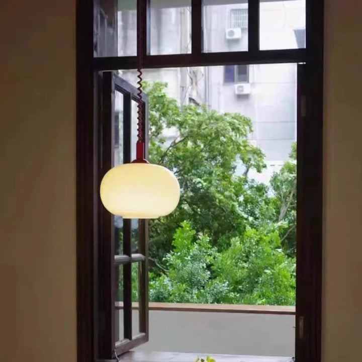 Suspension luminaire pendira avec verre blanc sphérique, cadre en bois foncé et câble spiralé rouge chaleureux