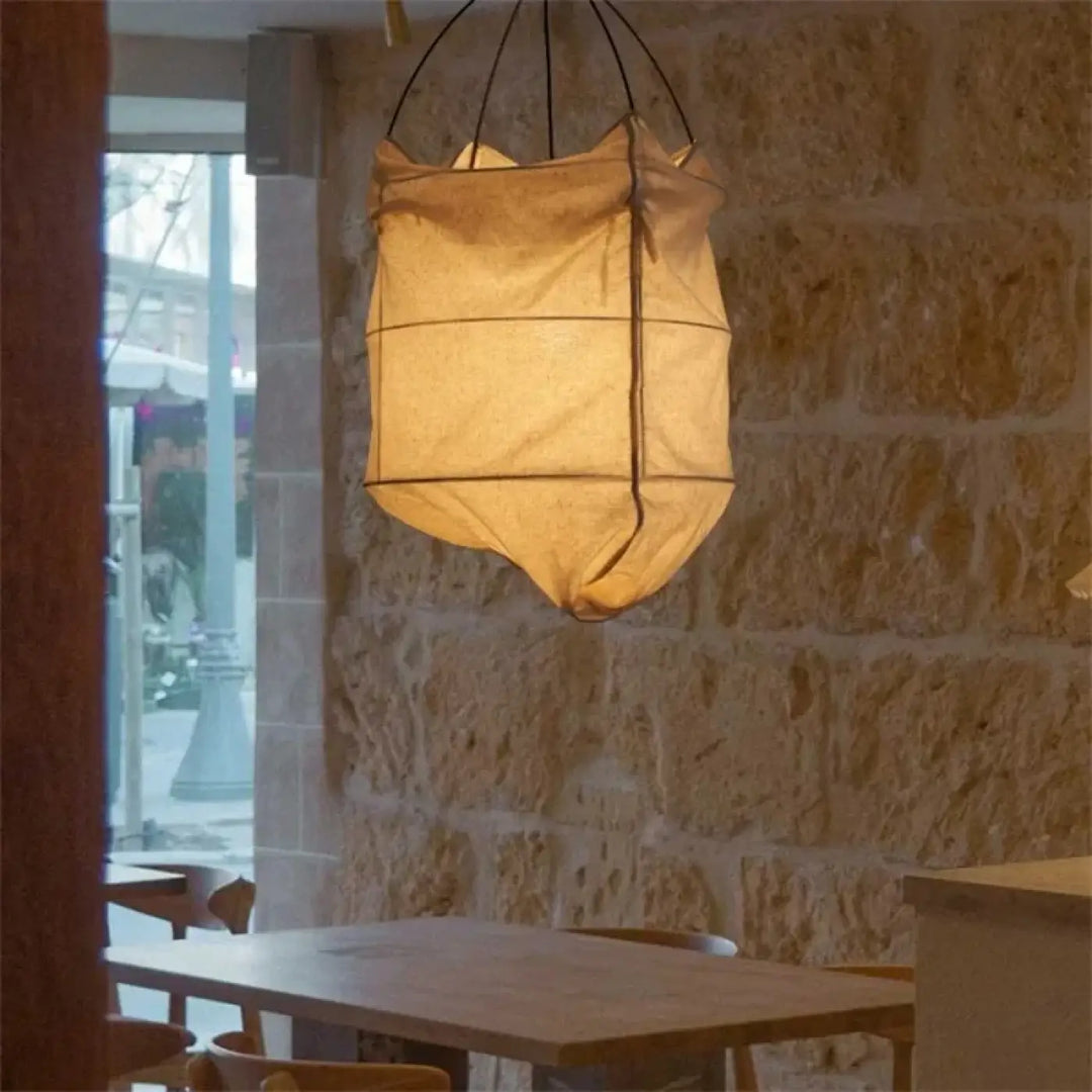 Suspension luminaire lima en tissu beige chaud avec style scandinave suspendue devant un mur en pierre rustique