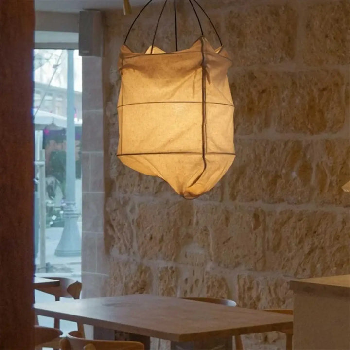 Suspension luminaire lima en tissu beige chaud avec style scandinave suspendue devant un mur en pierre rustique