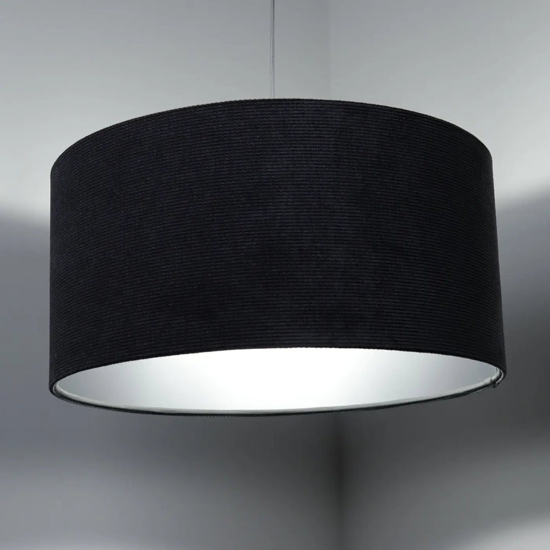 Suspension luminaire with tissu graphite cylindrical lampshade textured exterior and silver reflective interior au-dessus d’une table