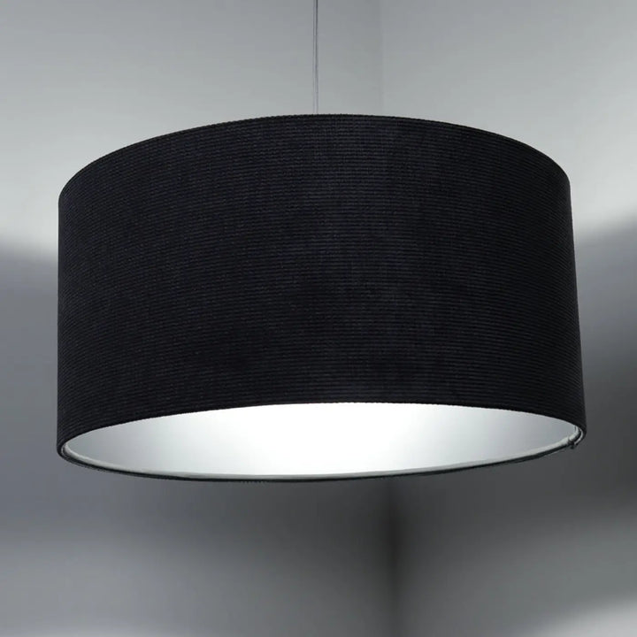 Suspension luminaire with tissu graphite cylindrical lampshade textured exterior and silver reflective interior au-dessus d’une table