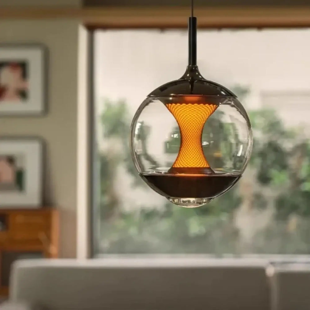 Suspension luminaire luma en verre sphérique avec tige en métal noir et diffuseur central lumineux orange émettant une lumière chaude