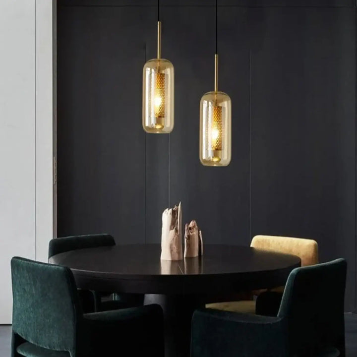 Deux suspension luminaires eloria dorées avec verre transparent aux nuances ambrées au-dessus d’une table en bois foncé