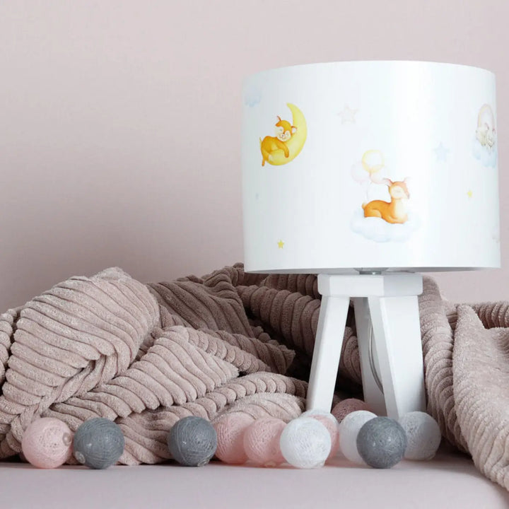 Lampe de table sweet dreams blanche avec abat-jour cylindrique illustré de cerfs sur lune et nuage sur pied trépied blanc