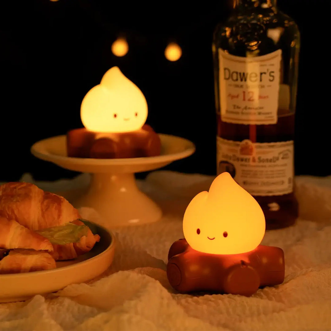 Veilleuse camp en forme de flamme jaune avec visage souriant posée sur des bûches pour une ambiance chaleureuse et camp cosy