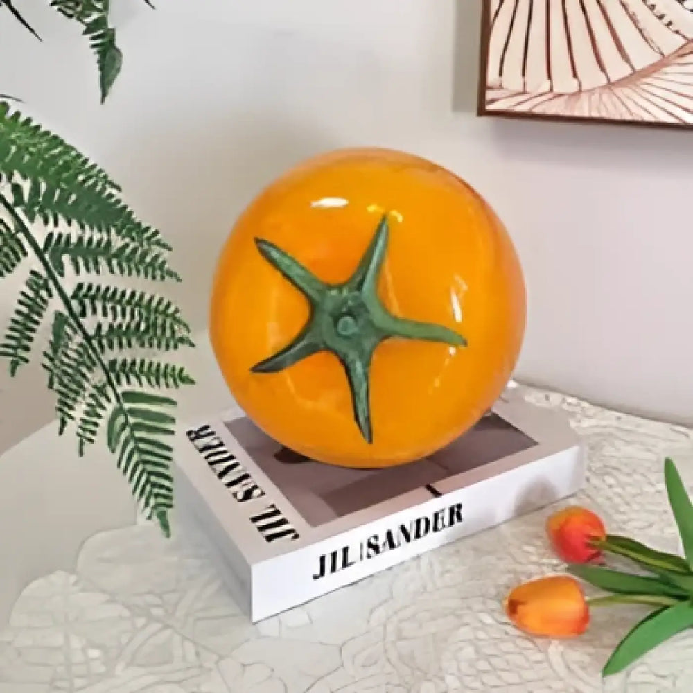 Veilleuse tomie orange brillante en forme de tomate avec création lumineuse apporte une ambiance douce sur un livre blanc