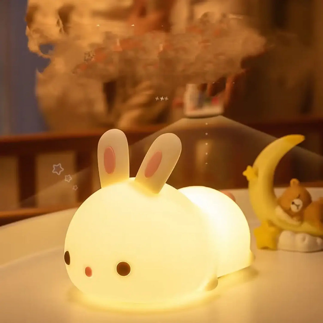 Veilleuse lapin souple blanche rabby avec oreilles roses et yeux noirs émettant une douce lumière sur une table
