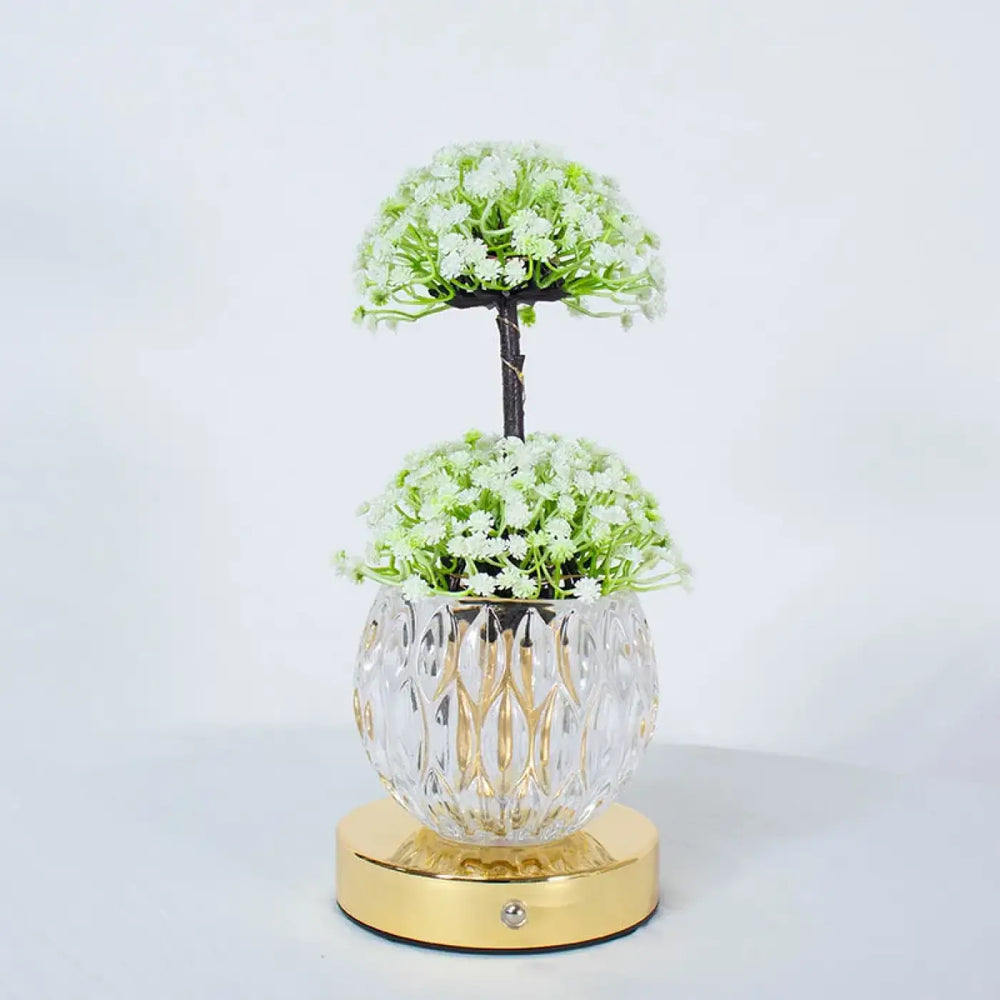 Lampe de table tulyna avec vase en verre facetté clair et base dorée tenant des fleurs blanches, source de lumière décorative