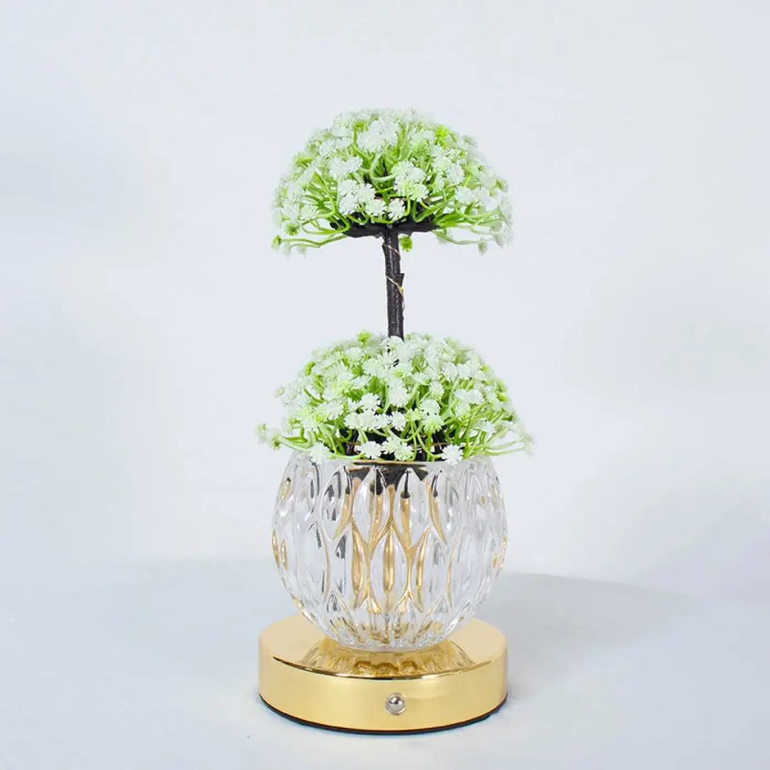 Lampe de table tulyna avec vase en verre facetté clair et base dorée tenant des fleurs blanches, source de lumière décorative