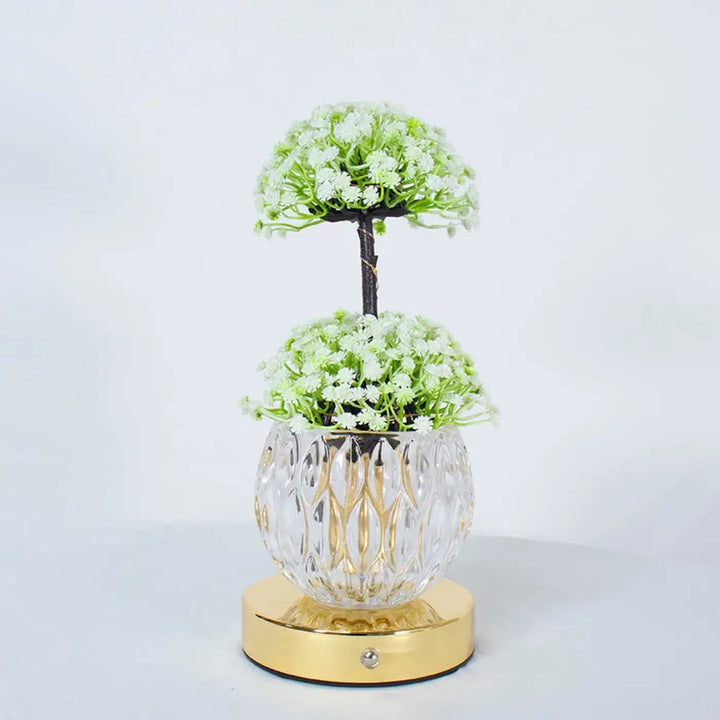 Lampe de table tulyna avec vase en verre facetté clair et base dorée tenant des fleurs blanches, source de lumière décorative