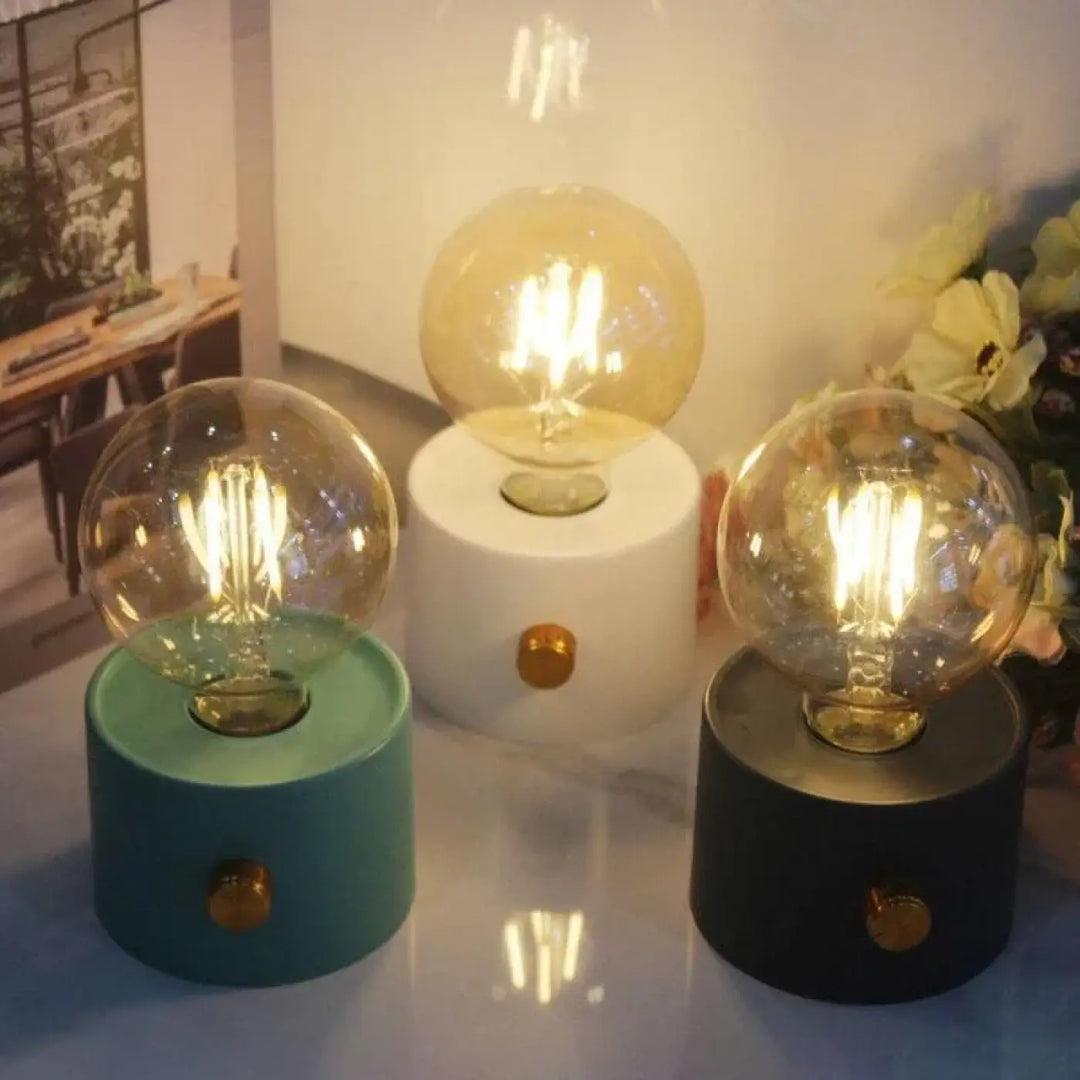 Veilleuse moderne monora avec ampoule apparente dans trois couleurs teal, blanc et noir sur socle cylindrique